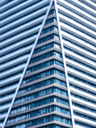 A modern high-rise building characterized by a sharp, angular design. The structure features numerous rows of windows, creating a pattern of glass and concrete. The prominent V-shape adds a dynamic and futuristic aesthetic.