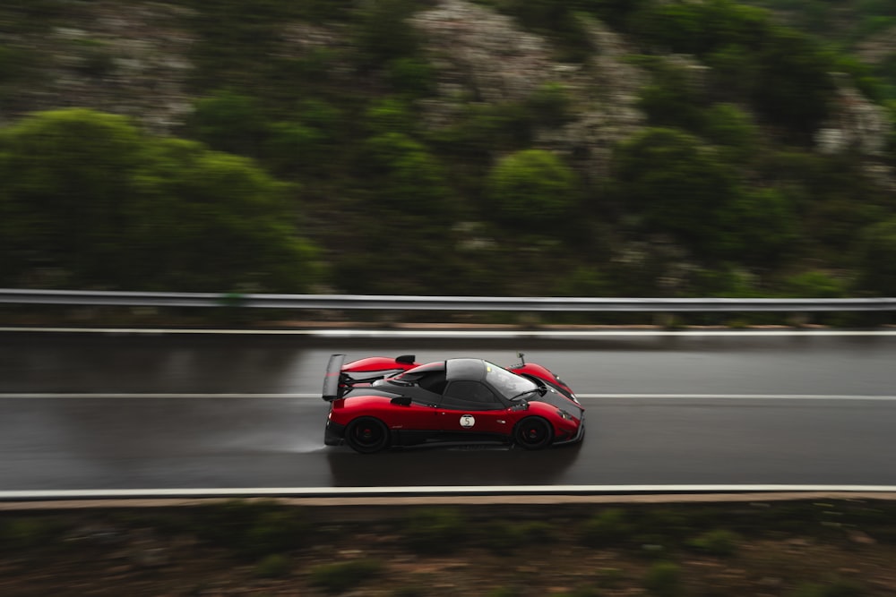 Un coche deportivo rojo conduciendo por una carretera mojada