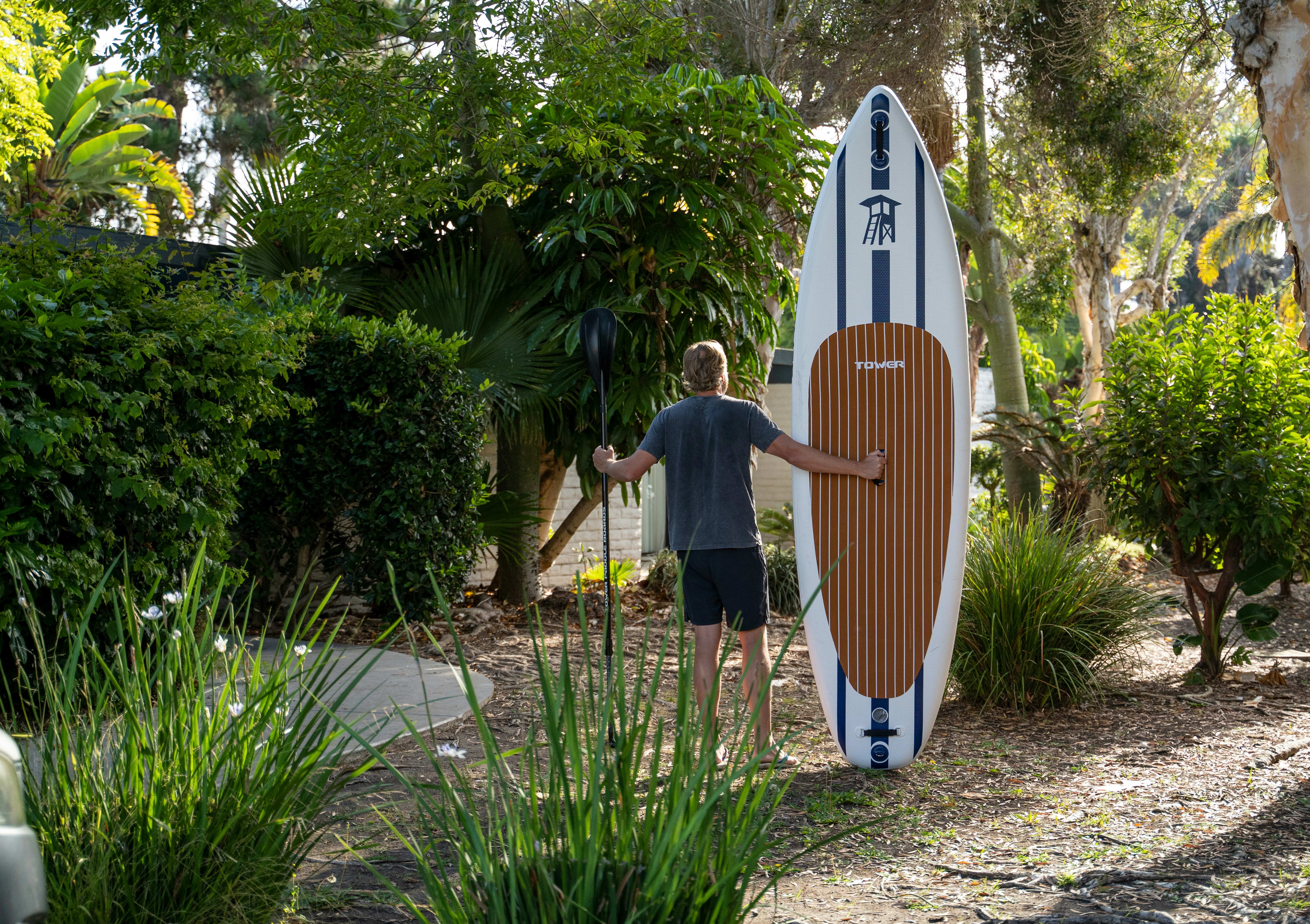 a man standing next to a surfboard in a garden