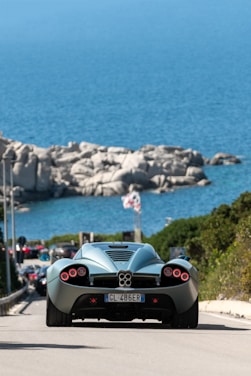 A sleek sports car being filmed by an influencer with a camera rig on a scenic coastal highway.