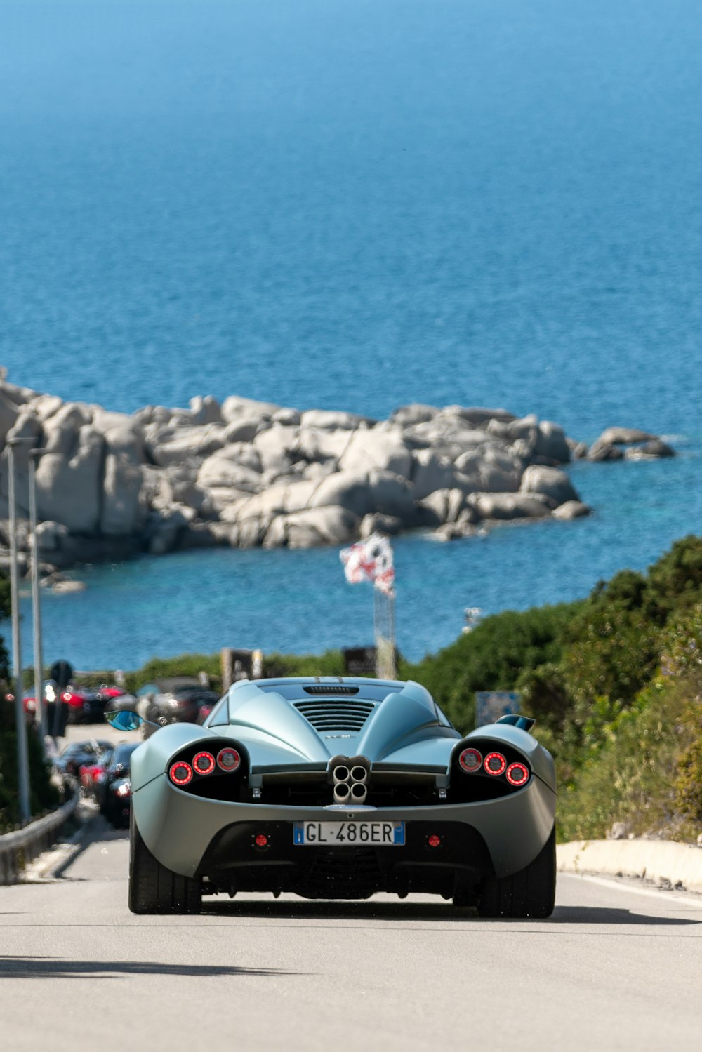 a blue sports car driving down a road next to the ocean