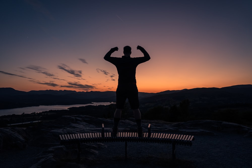 a man standing on top of a bench at sunset