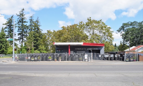 A roadside tire shop with various tires displayed and a friendly mechanic ready to assist customers.