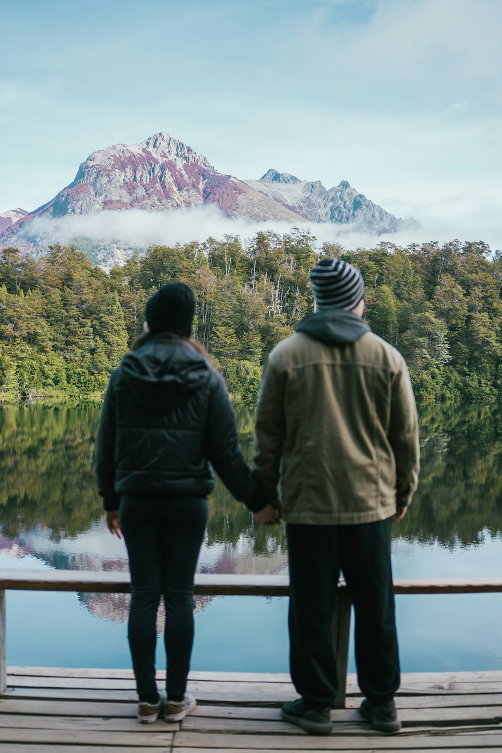 two people standing on a dock looking at a lake