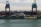 A large cargo ship named Oldendorff is docked at an industrial port. Two towering cranes stand above the ship, indicating loading or unloading activities. In the background, there are large piles of materials, possibly coal or gravel, with industrial buildings and storage tanks visible under an overcast sky.