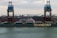 A large cargo ship named Oldendorff is docked at an industrial port. Two towering cranes stand above the ship, indicating loading or unloading activities. In the background, there are large piles of materials, possibly coal or gravel, with industrial buildings and storage tanks visible under an overcast sky.