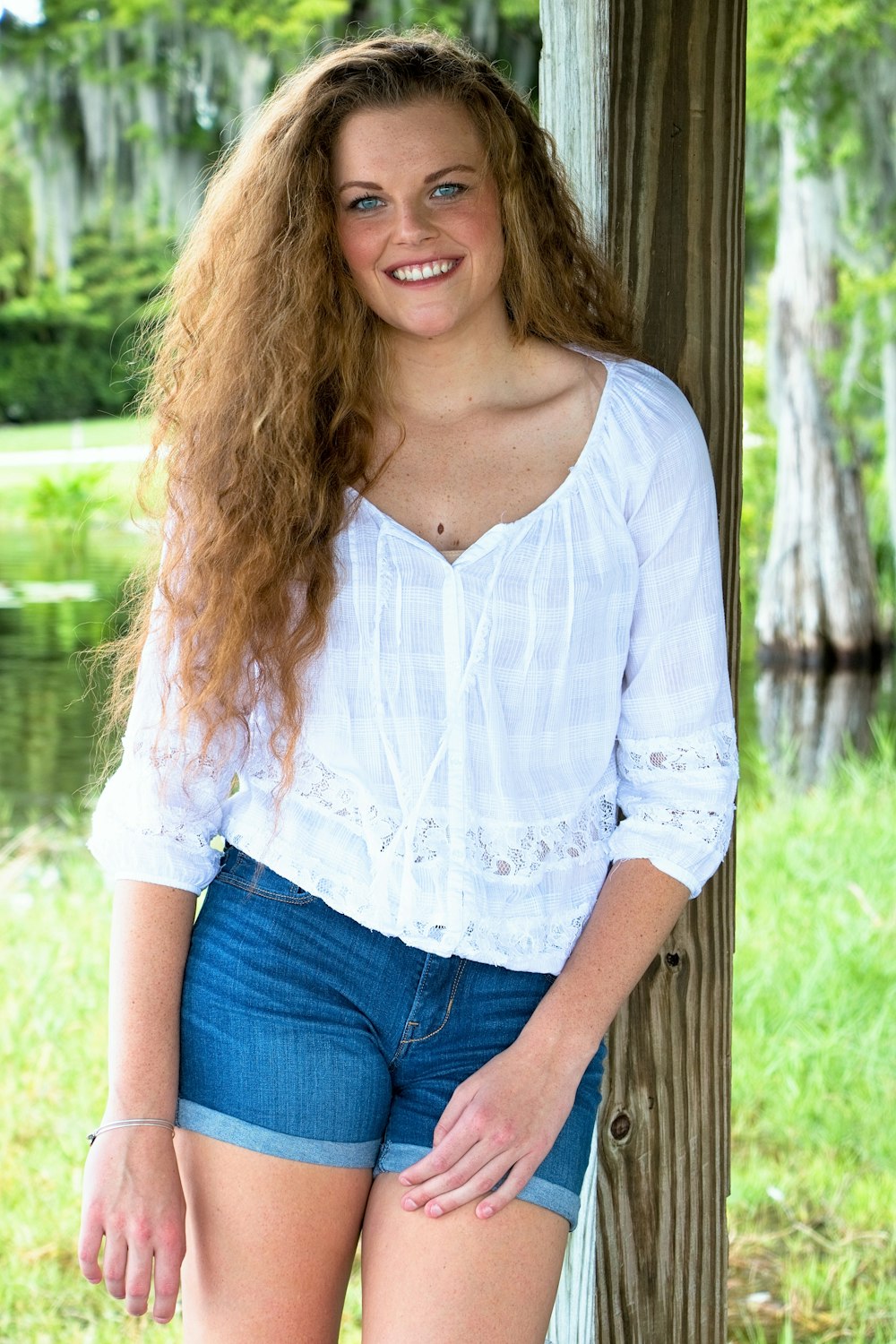 a beautiful young woman standing next to a tree