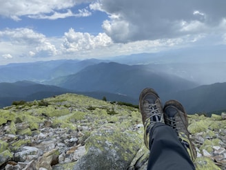 A pair of durable hiking boots dusted with trail dirt, sitting at the edge of a mountain overlook.