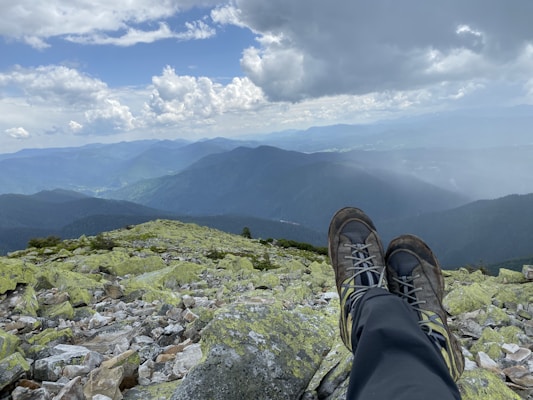 A pair of durable hiking boots dusted with trail dirt, sitting at the edge of a mountain overlook.