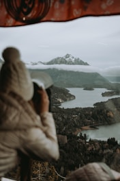 a person looking out a window at a lake and mountains