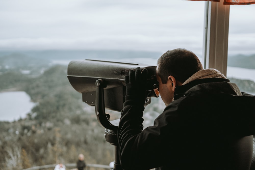 a man looking through a telescope at a scenic view