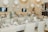 A beautifully arranged table setting in an elegant venue, featuring white tablecloths, beige napkins, and floral centerpieces in sleek vases. The background includes white balloons and soft lighting, creating a sophisticated ambiance.