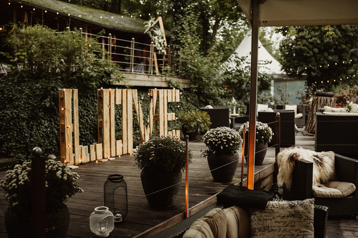 Wood deck with patio seating, planter pots, and a landscaped tree-and-shrub border wrapping the space