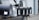 A row of six black mailboxes is mounted on a metal beam. Each mailbox is labeled with a white letter from A to F. The background includes part of a vehicle and a chain-link fence.