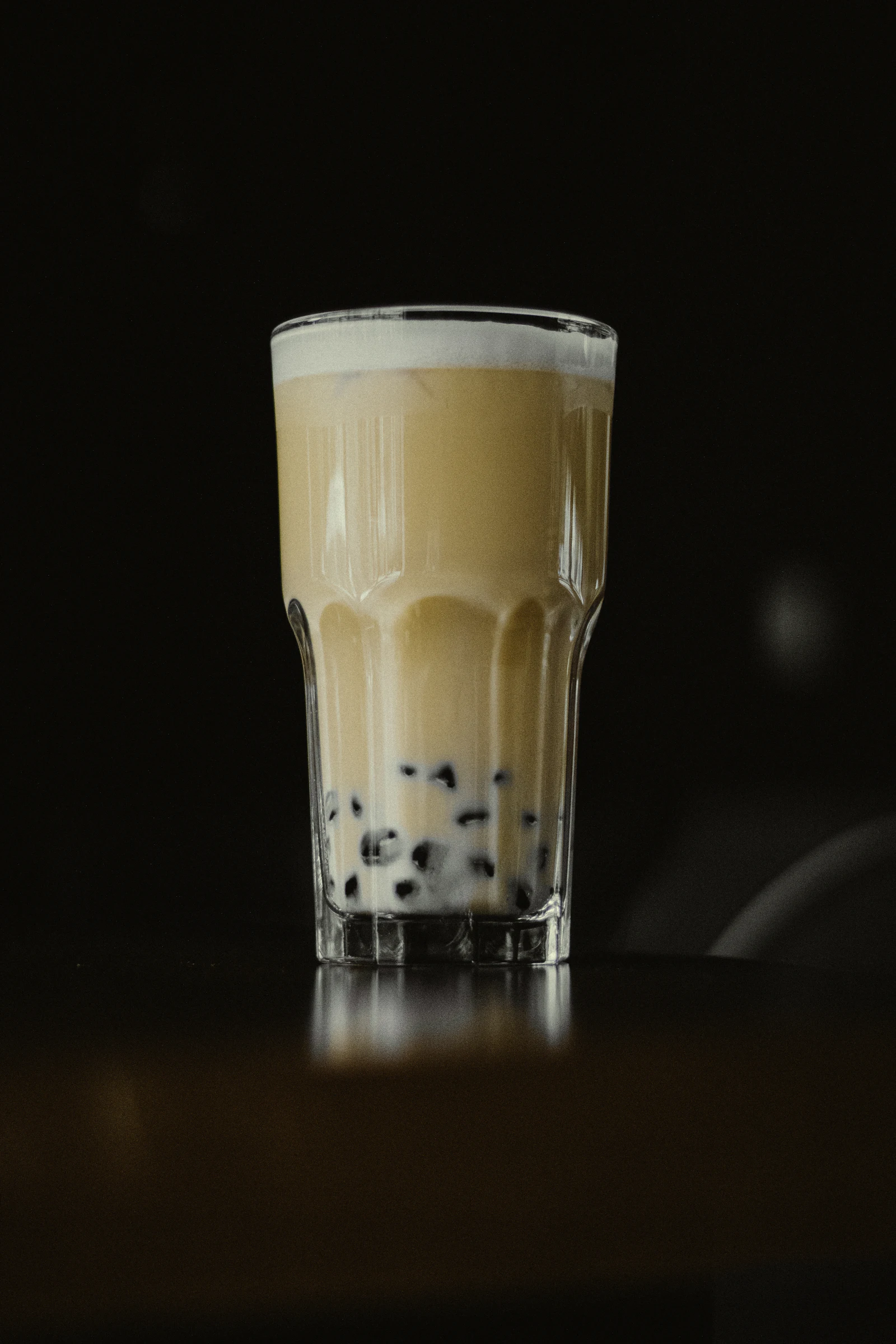 A glass of milk tea with dark tapioca pearls settled at the bottom against a black background