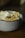A close-up of a bowl filled with tortilla chips, a fried egg, and some kind of creamy white sauce or cheese. Garnished with herbs, the dish is placed on a wooden surface.