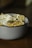A close-up of a bowl filled with tortilla chips, a fried egg, and some kind of creamy white sauce or cheese. Garnished with herbs, the dish is placed on a wooden surface.