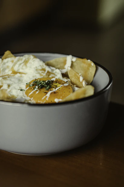 Close-up of a gourmet Spanish tortilla topped with vibrant piquillos and fresh herbs on a rustic wooden board.