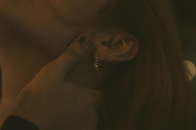 A close-up of a person's ear adorned with a hoop earring featuring small decorative elements. A hand with painted nails is gently cupping the ear.