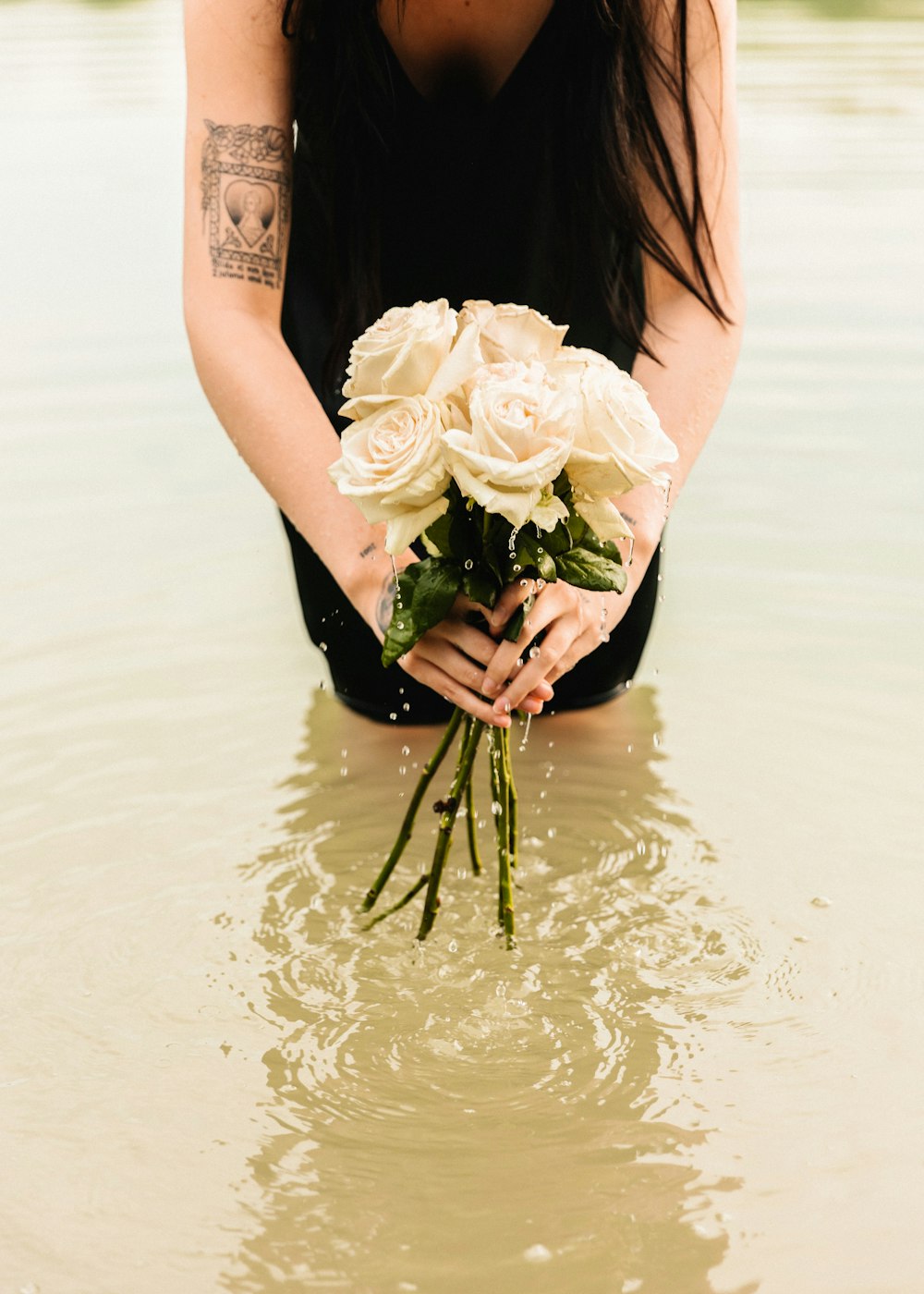 uma mulher ajoelhada na água segurando um buquê de flores