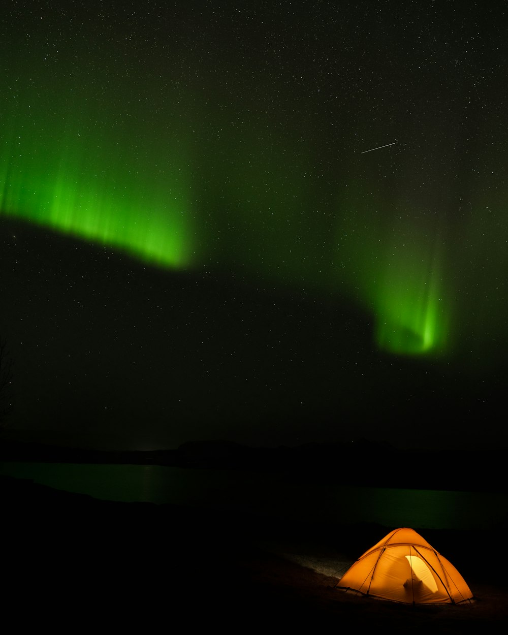 a tent is lit up in the dark with the aurora lights in the background