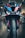 A close-up view of a high-performance motorcycle featuring an aggressive front design with sharp headlights and a colorful body with black, blue, red, and orange details. The image captures the bike's front tire, aerodynamic components, and a part of the showroom in the background.