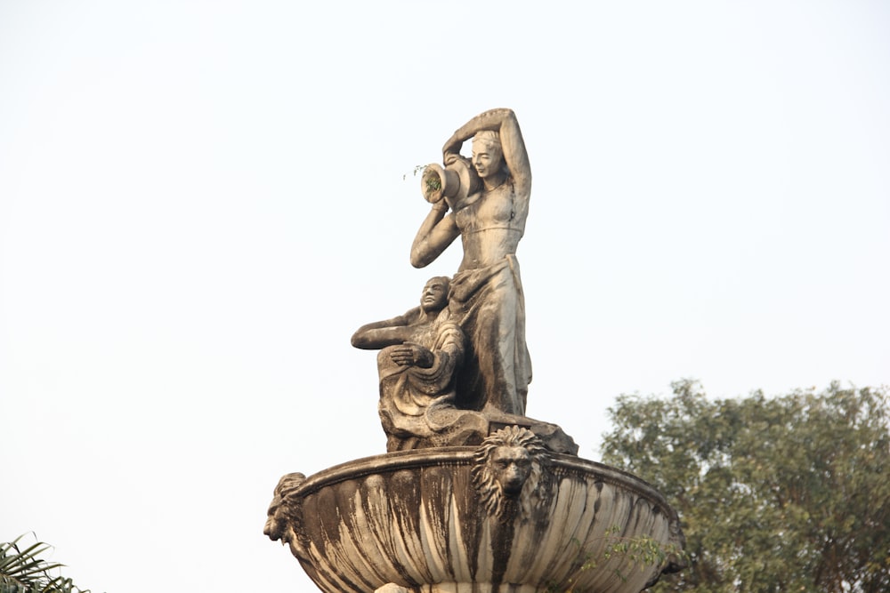 une statue d’une femme tenant un oiseau au sommet d’une fontaine
