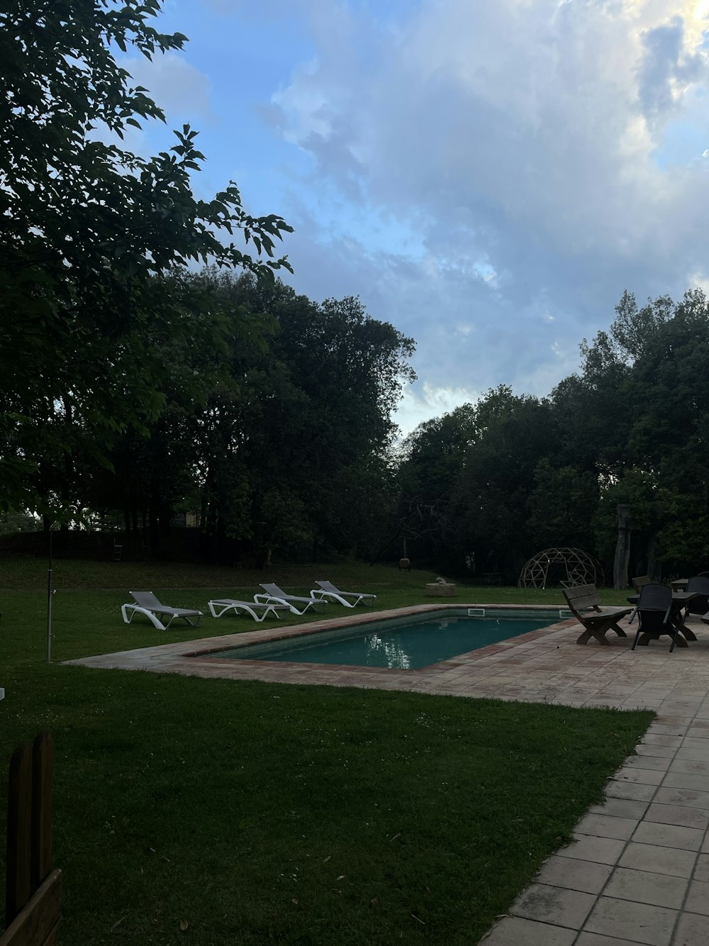 a pool surrounded by lawn chairs and trees