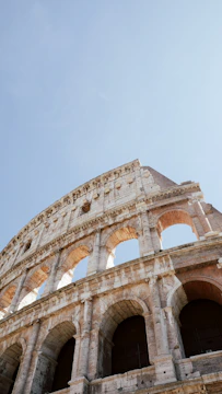 A close-up of the ancient Roman Colosseum’s weathered stone arches under a bright blue sky.
