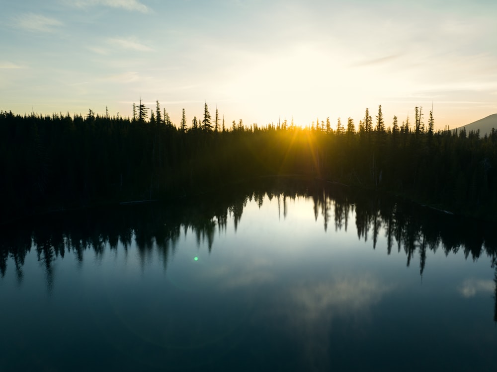 the sun is setting over a lake surrounded by trees