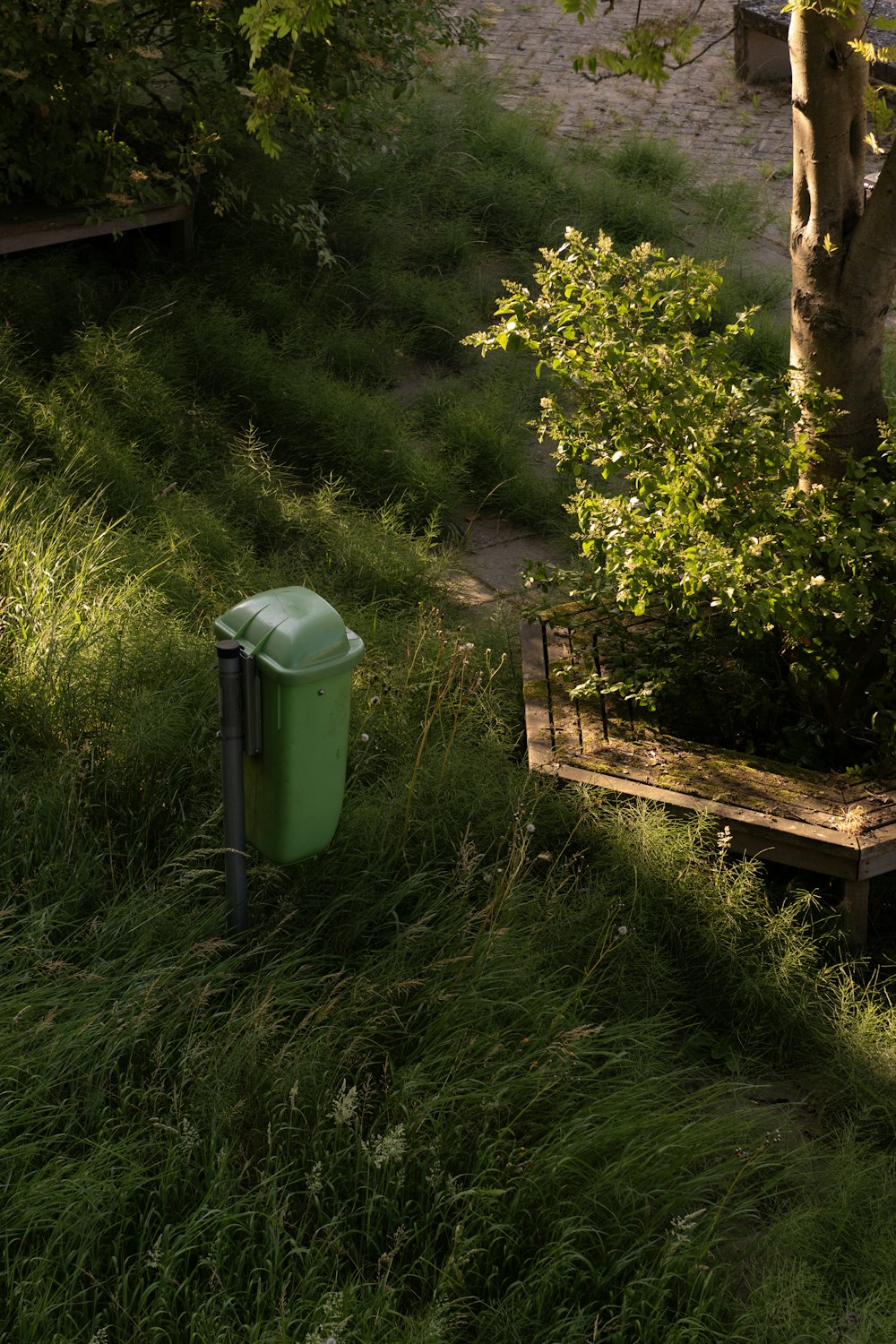 a trash can sitting in the grass next to a bench