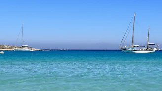 The sailboat Paradisean anchored peacefully in a turquoise bay under a clear blue sky.