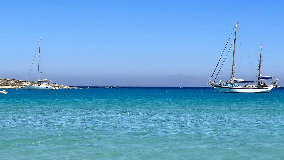 The sailboat Paradisean anchored peacefully in a turquoise bay under a clear blue sky.