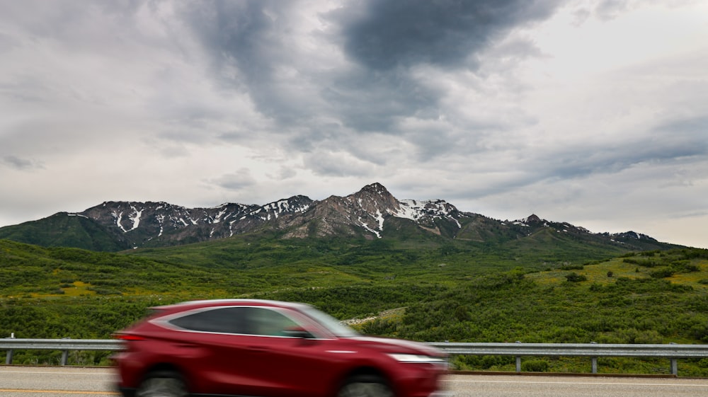a red car driving down a road with mountains in the background