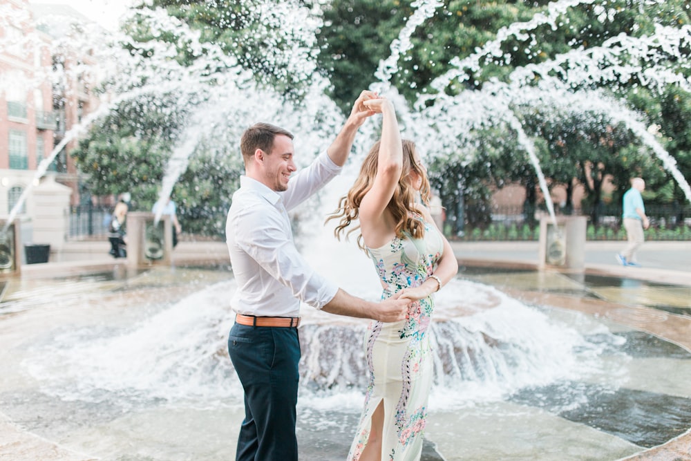 a man and woman dancing in front of a fountain