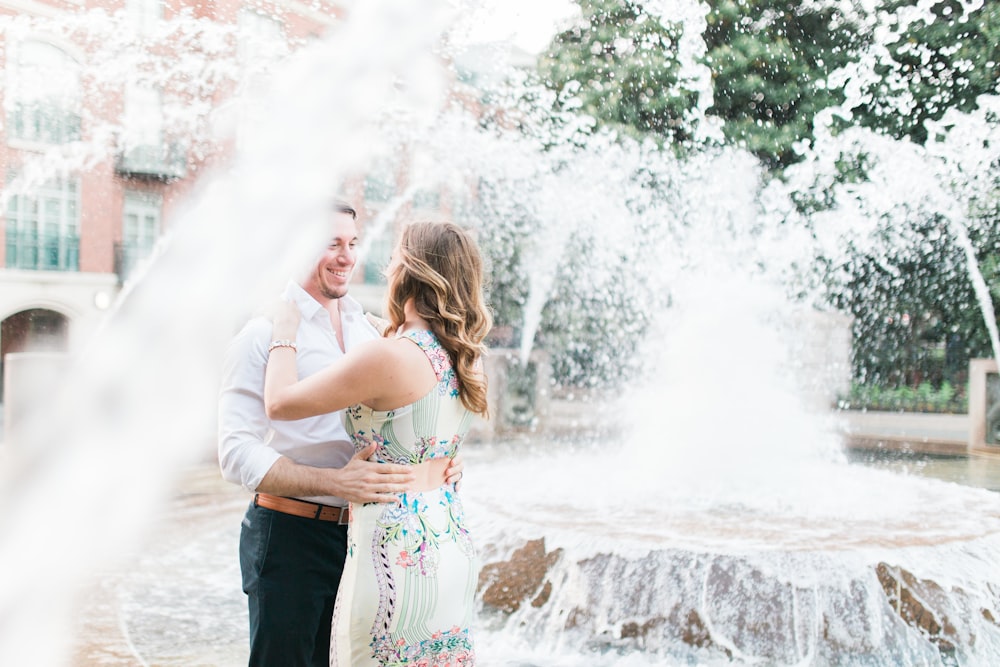 a man and woman standing in front of a fountain