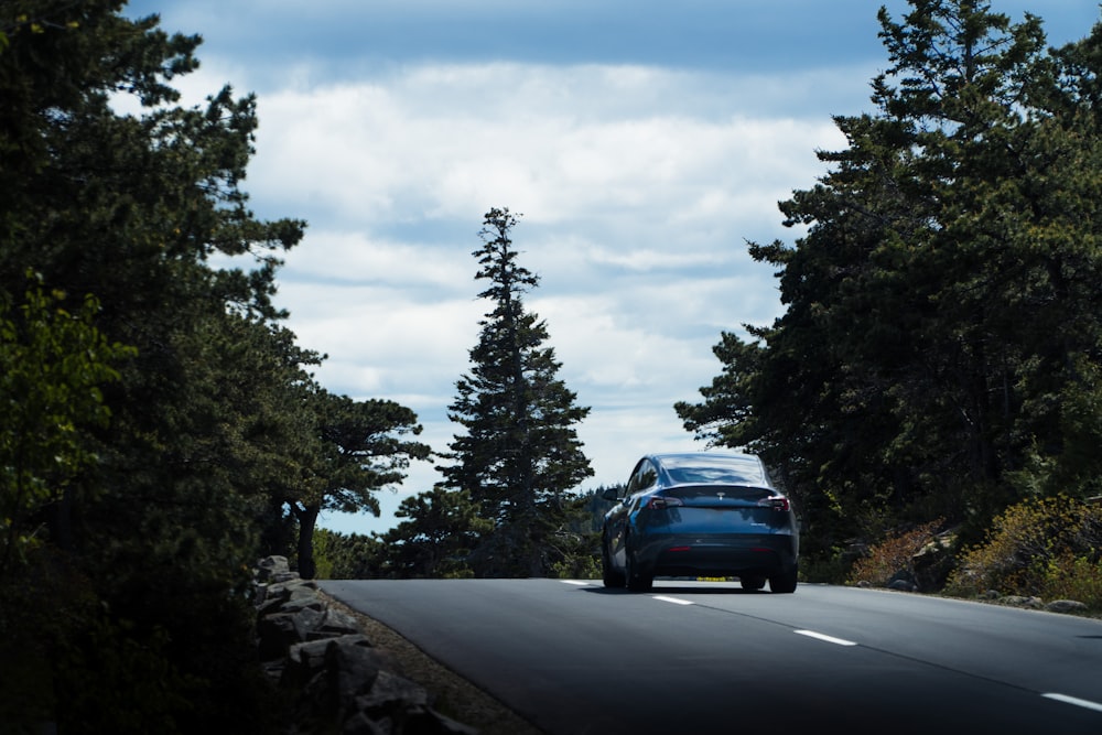 a blue car driving down a road surrounded by trees