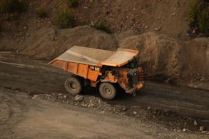 an orange dump truck driving down a dirt road
