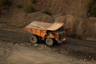 Brightly colored end dump truck driving along a dusty road with a full load of dirt.