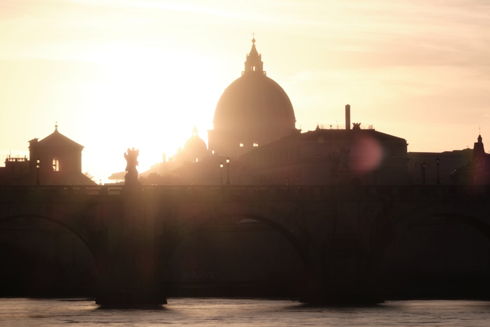 the sun is setting over a bridge with a building in the background