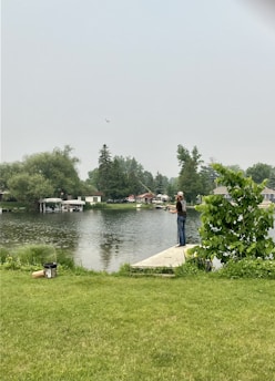 A beginner angler casting a line into a calm suburban lake surrounded by trees.
