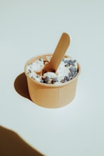 Close-up of a premium 5-ounce transparent disposable cup filled with creamy artisanal ice cream in a beige and olive green setting.