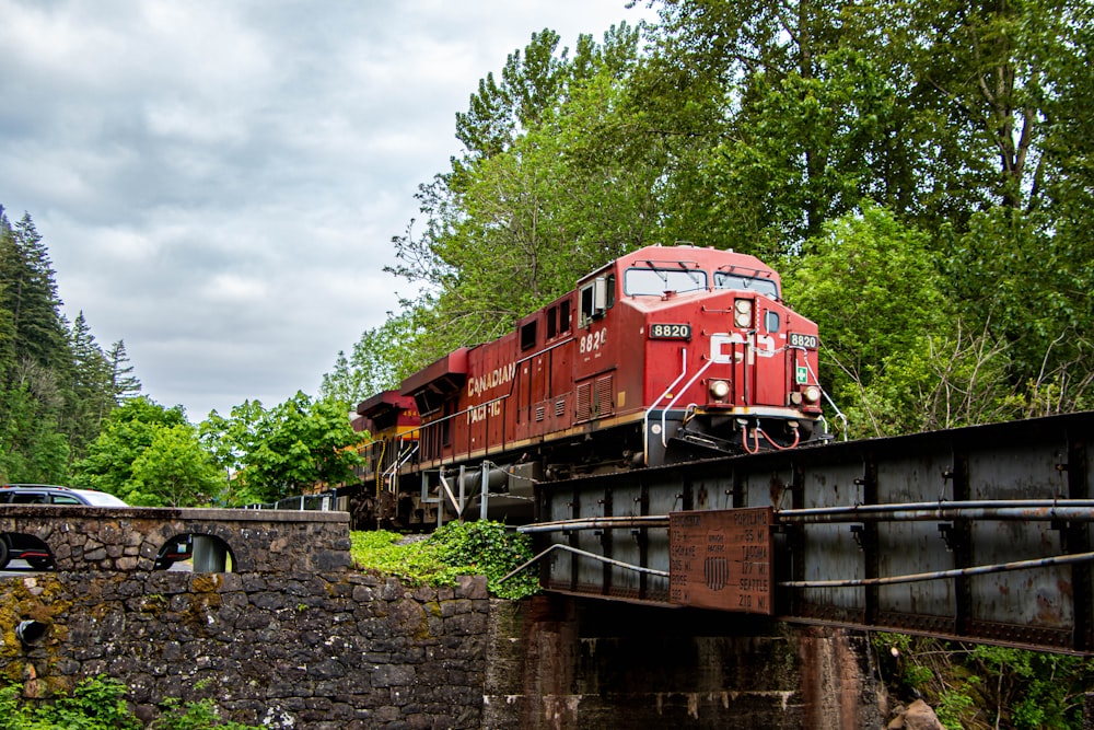 a red train traveling over a bridge next to a forest