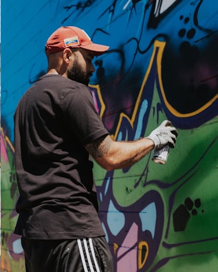 A street artist painting a mural while wearing a Rainbow Collections cap.