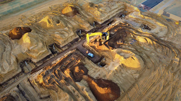 A heavy excavator digging earth on a bright sunny day at a road construction site.