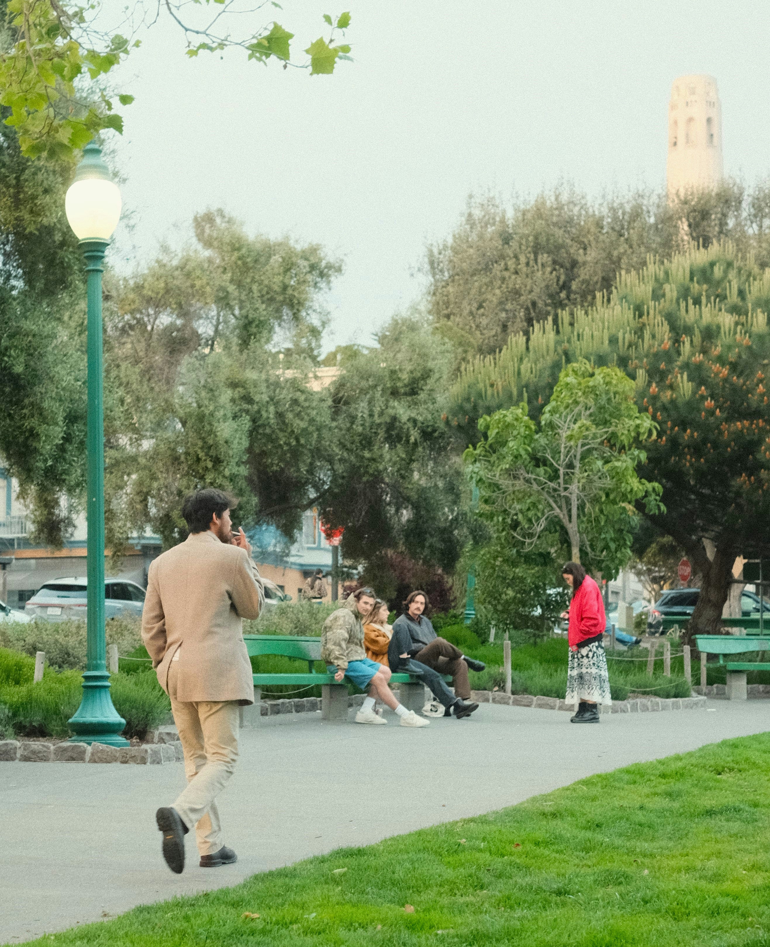 a man walking down a sidewalk next to a lush green park