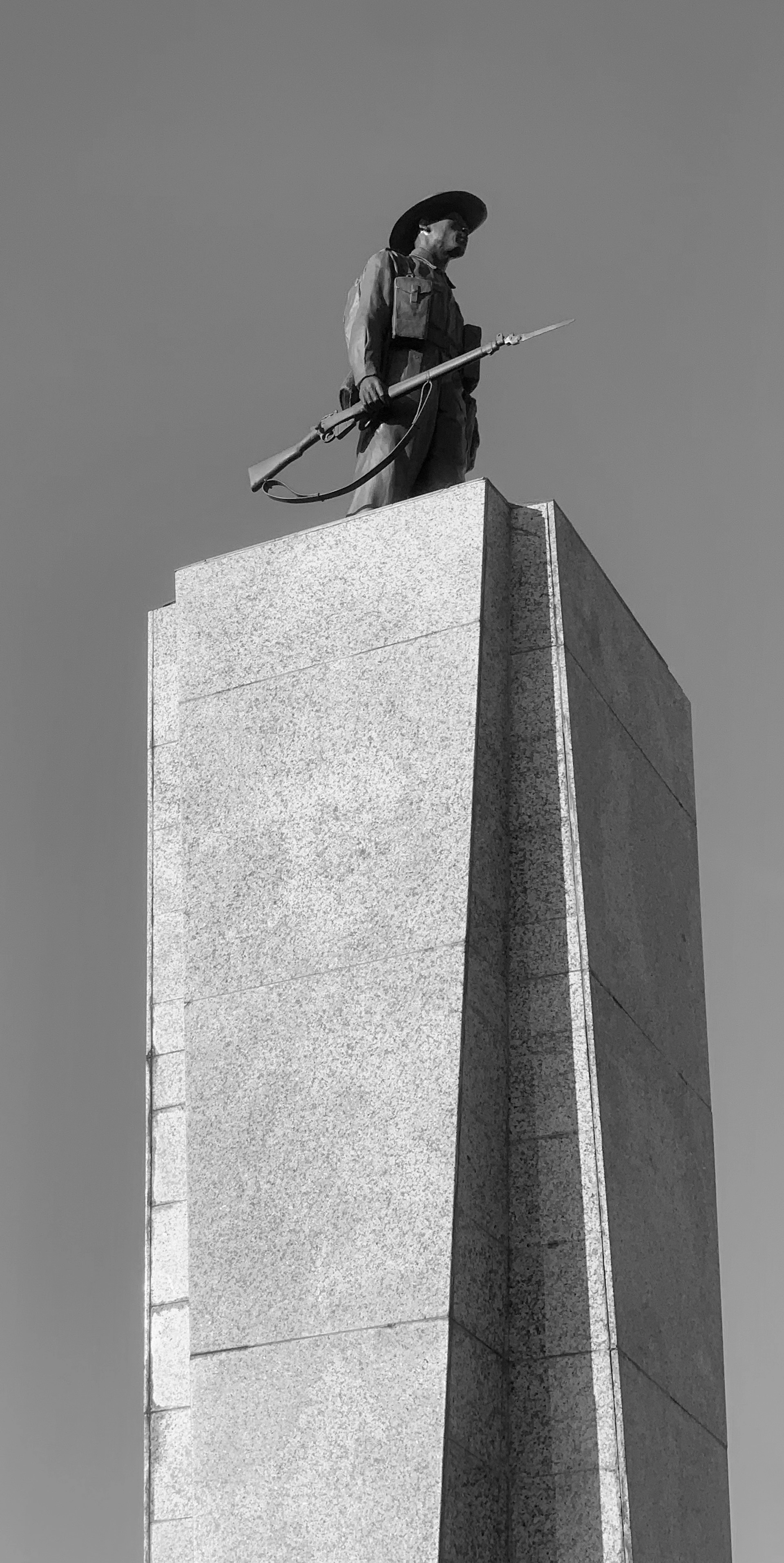 Black-and-white low-angle view of a soldier statue with rifle and bugle atop a tall granite memorial column.