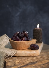 a wooden bowl filled with plums next to a lit candle