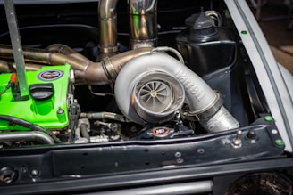 A car engine bay featuring a prominent Garrett turbocharger with polished metal components. Nearby, there is a vivid green engine component with labels. Various pipes and engine parts are visible, highlighting detailed automotive engineering.