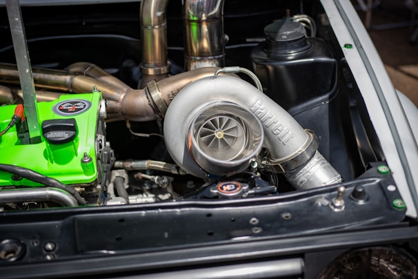 A car engine bay featuring a prominent Garrett turbocharger with polished metal components. Nearby, there is a vivid green engine component with labels. Various pipes and engine parts are visible, highlighting detailed automotive engineering.